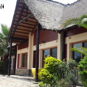 Strohgedeckte Gästevillen, gesäumt von Palmen, entlang eines gepflasterten Wegs im Kansanshi Hotel, Solwezi