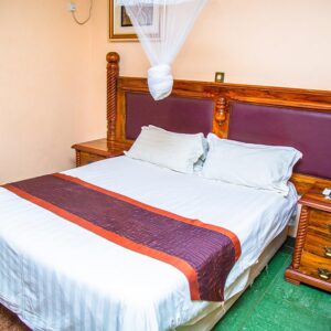 A guest room at Crossroads Lodge in Chipata, with a wooden four-poster bed and mosquito net