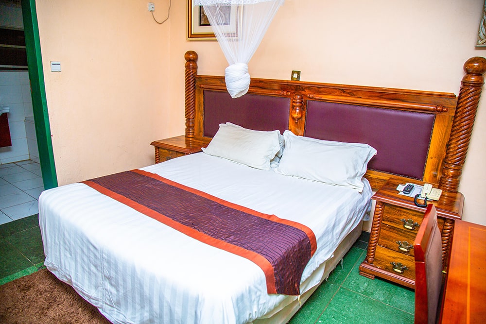 A guest room at Crossroads Lodge in Chipata, with a wooden four-poster bed and mosquito net