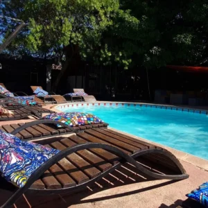 Lettini con cuscini fantasia accanto alla piscina ombreggiata dell’ostello di Livingstone che ora opera come Victoria Falls Backpackers Zambia