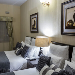 A twin guest room at the Mokorro Hotel in Chingola, with two beds in white linen and framed prints above them