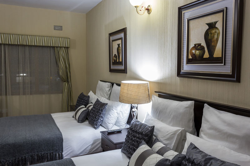 A twin guest room at the Mokorro Hotel in Chingola, with two beds in white linen and framed prints above them
