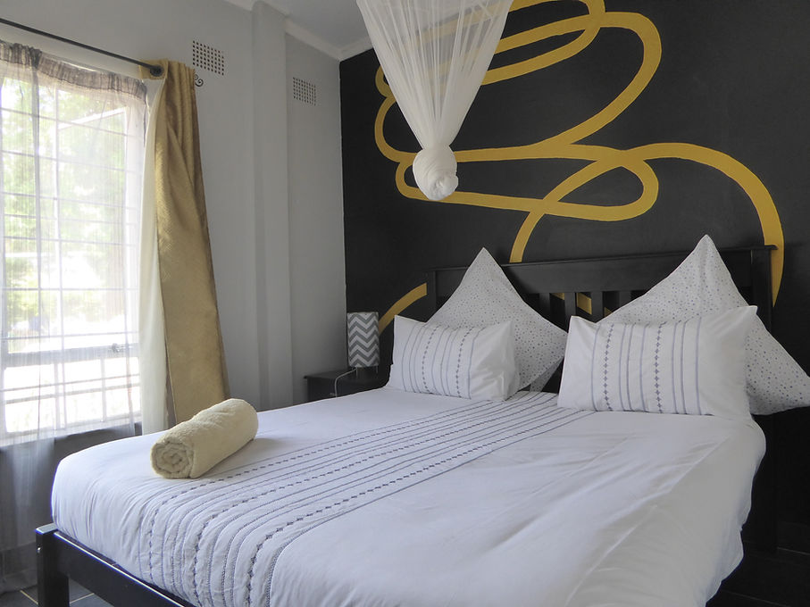 Une chambre twin privative au Natwange Backpackers à Lusaka, avec une moustiquaire drapée et un mur décoratif peint