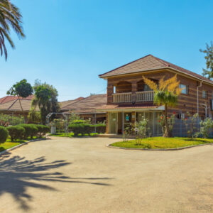 The two-storey timber-clad main building of Tecla Lodge in Lusaka, seen from its palm-lined driveway