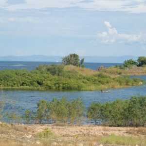 A grassy islet and the open water of Lake Kariba seen from the Zambian shore near Siavonga. Context photograph of the area around Lake Safari Lodge, not of the property itself.