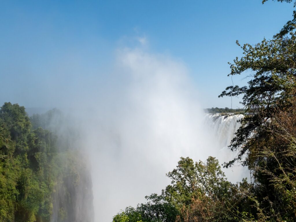 The curtain of Victoria Falls in full spray viewed from the Zambian bank of the Zambezi